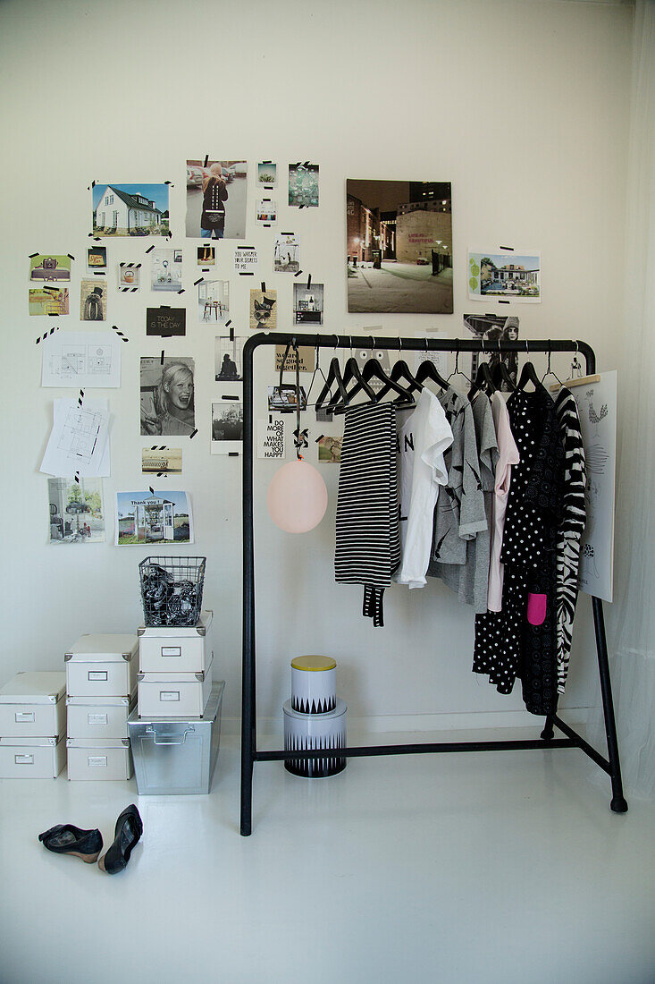 Black clothes rail next to storage boxes on white floor below magazine cuttings and postcards stuck to wall with washi tape