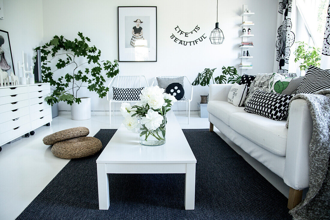 Black and white colour scheme combined with green houseplants - white coffee table on black rug and patterned scatter cushions on sofa