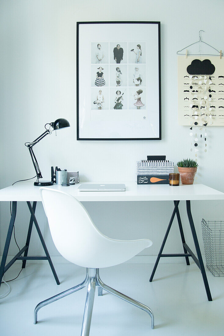 White swivel chair and desk on black trestles below framed picture on wall of study