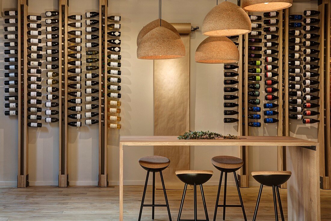 Weingeschäft mit reduzierter Holztheke, Barhockern, Lampenschirmen aus Kork und Weinflaschen in modernem Regalsystem