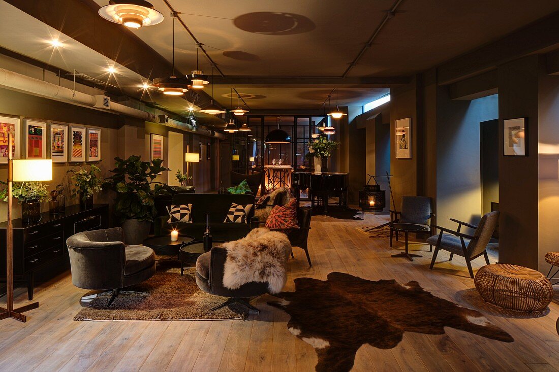 Grossräumige Lounge mit verschiedenen beleuchteten Sitzbereichen auf rustikalem Dielenboden und Tierfellen, gemütliche Atmosphäre