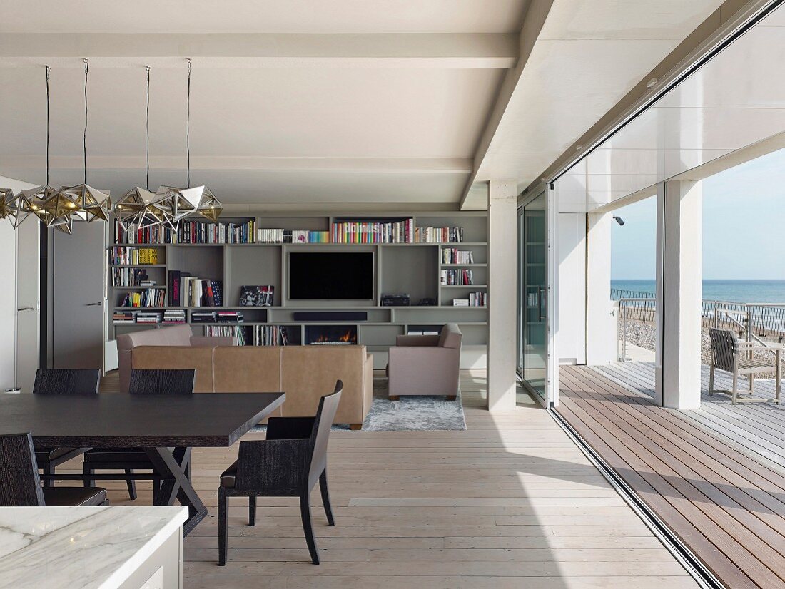 Offener Wohnraum mit Essplatz und Loungebereich vor offener Terrassentür mit Meerblick