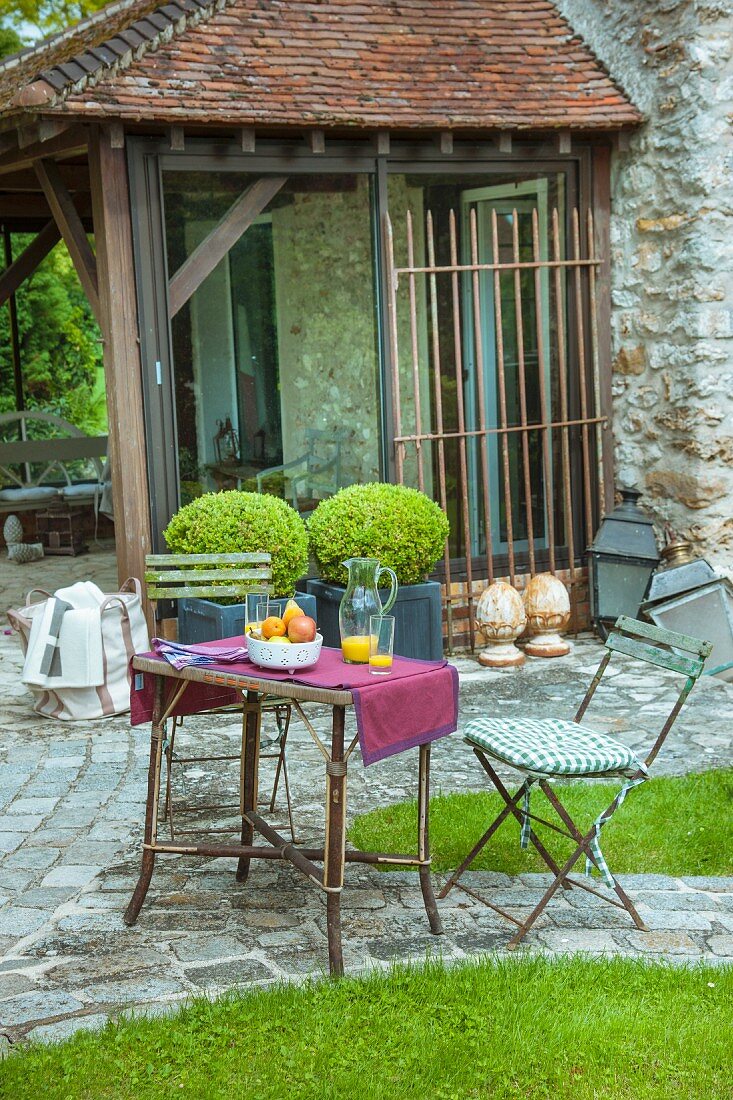 Gartentisch mit Stühlen, im Hintergrund Buchsbaumkugeln in Pflanzgefäss vor überdachter Terrasse