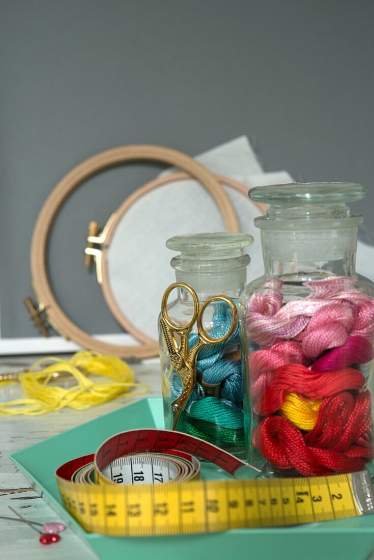 An arrangement of embroidery utensils: an embroidery frame, thread and a measuring tape