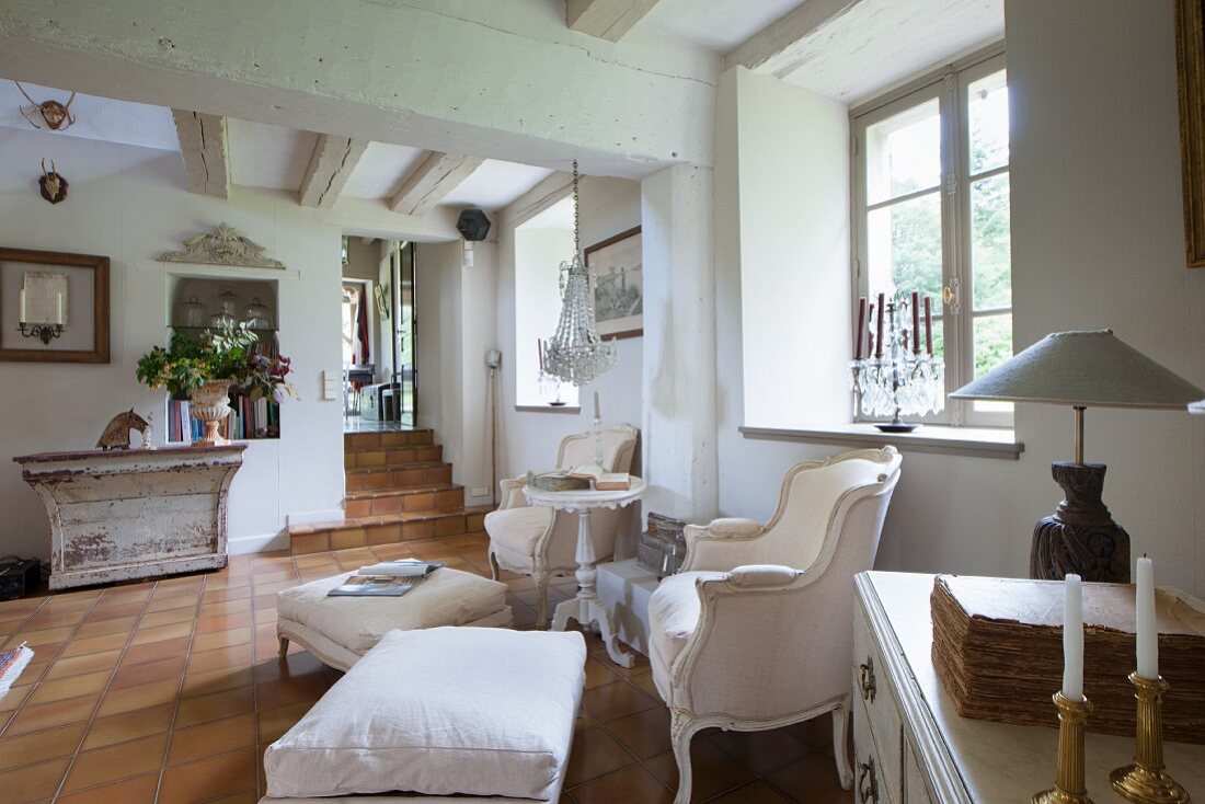 Zwei Rokoko Sessel und Fussschemel mit hellem Bezug am Fenster in ländlichem Wohnzimmer mit Terrakottafliesenboden