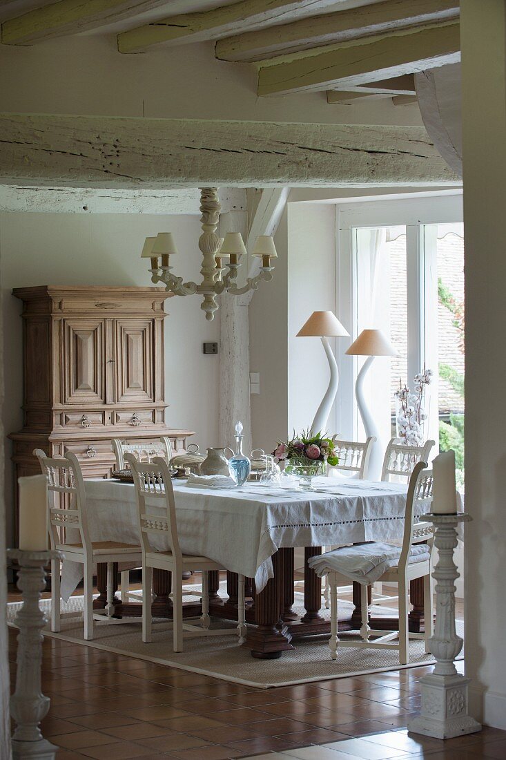 White dining set, chairs with carved backrests and designer table lamps in front of window in background