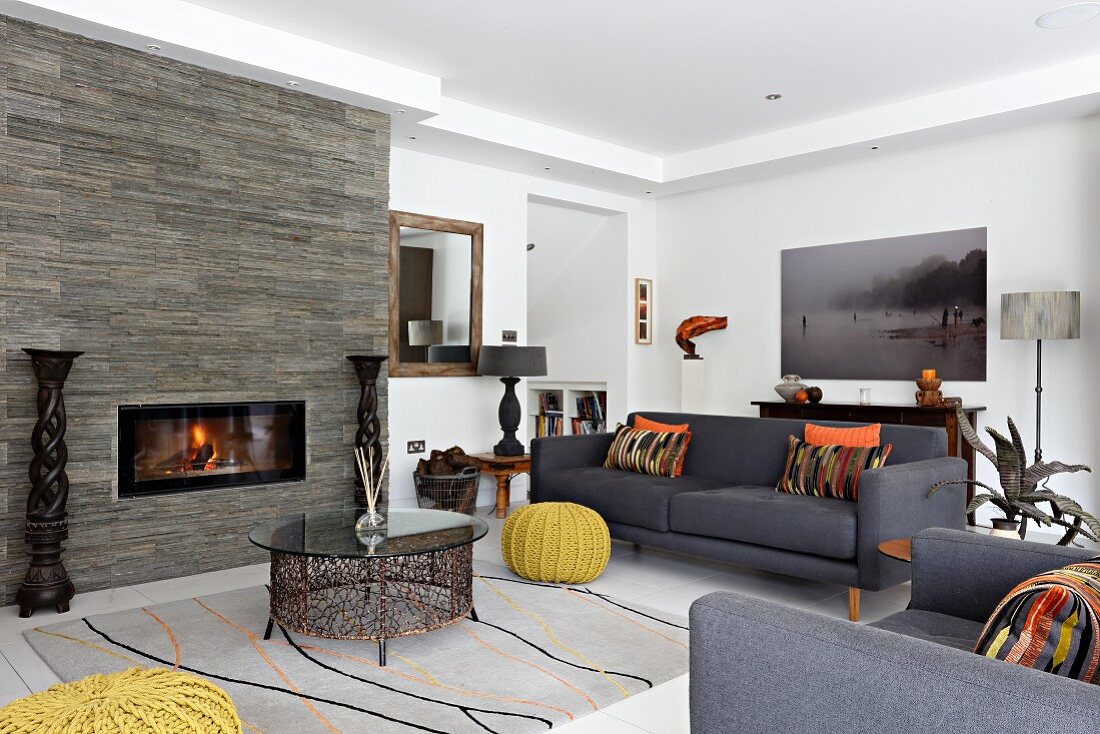 Colourful scatter cushions on grey sofa set and ethnic accessories around fireplace in stone wall