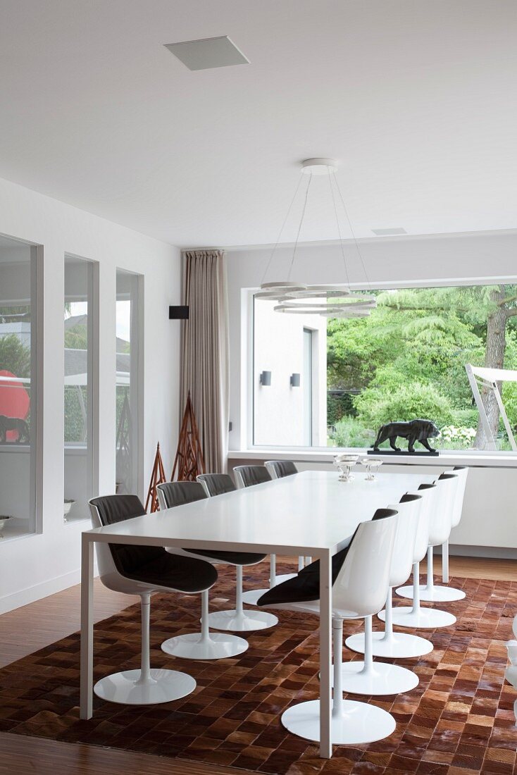 Designerstühle und minimalistischer Esstisch auf Tierfell-Patchworkteppich, Designerleuchte und Kunstobjekte vor Fenster