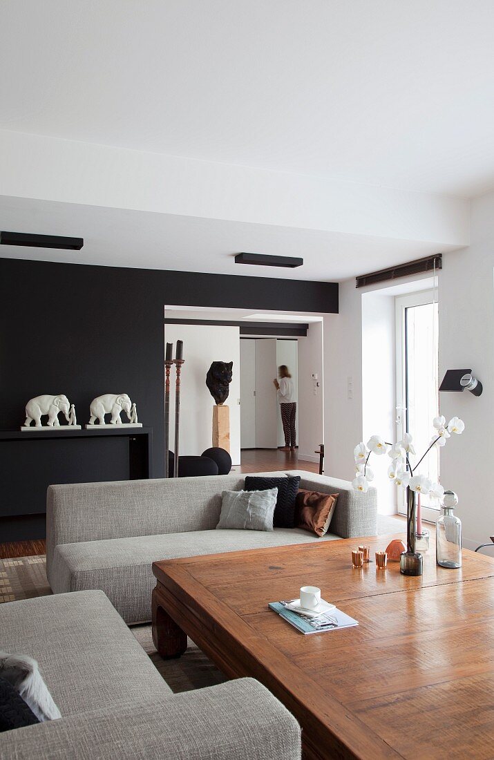 Moderner Wohnraum mit Sofagarnitur und wuchtigem Kolonialtisch, Kunstobjekte und Elefantenfiguren im Hintergrund