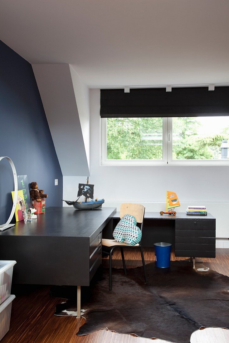 Black, L-shaped desk below dormer window and animal-skin rug in study