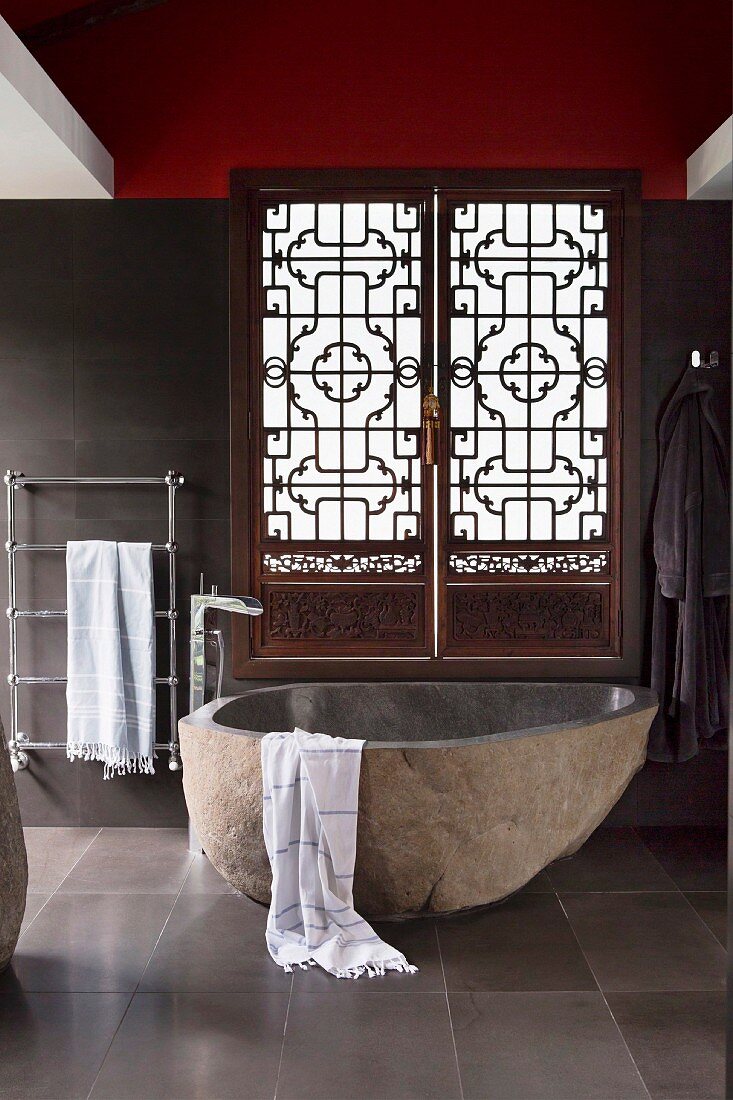 Badewanne aus naturbelassenem Stein vor geschnitzten Fensterläden in asiatischem Stil