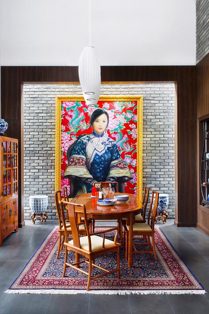Fine wood dining table and chairs in front of gold frame picture with Asian woman motif on light brick wall