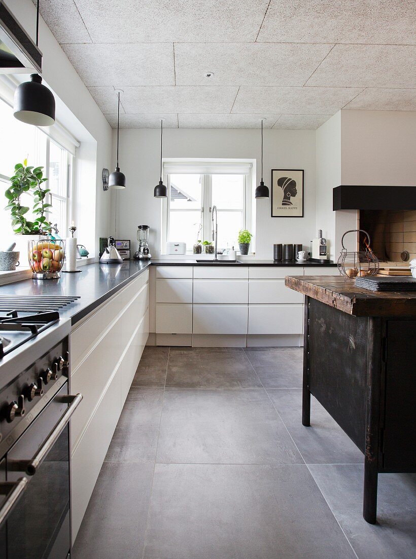 White L-shaped kitchen counter, black pendant lamps and island counter made from old workbench