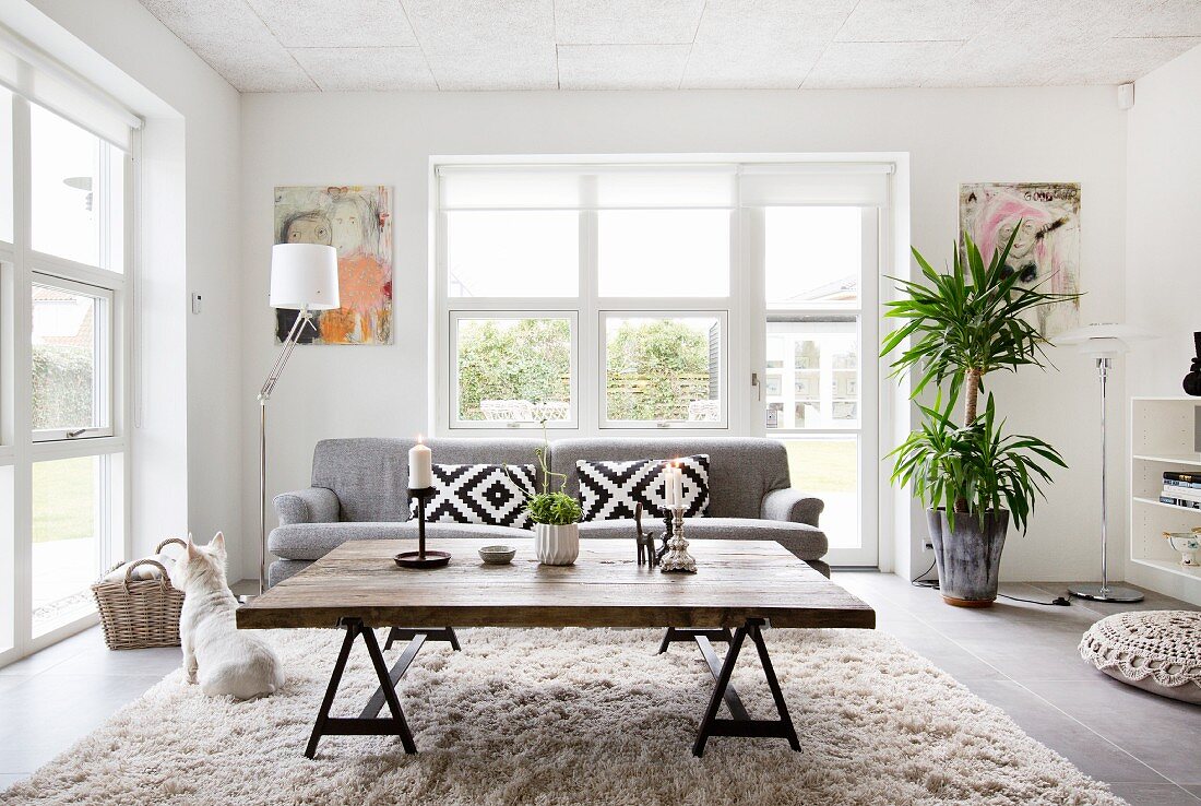 Rustikaler Couchtisch aus recyceltem Holz und graue Couch vor Terrassenfenster im Wohnzimmer