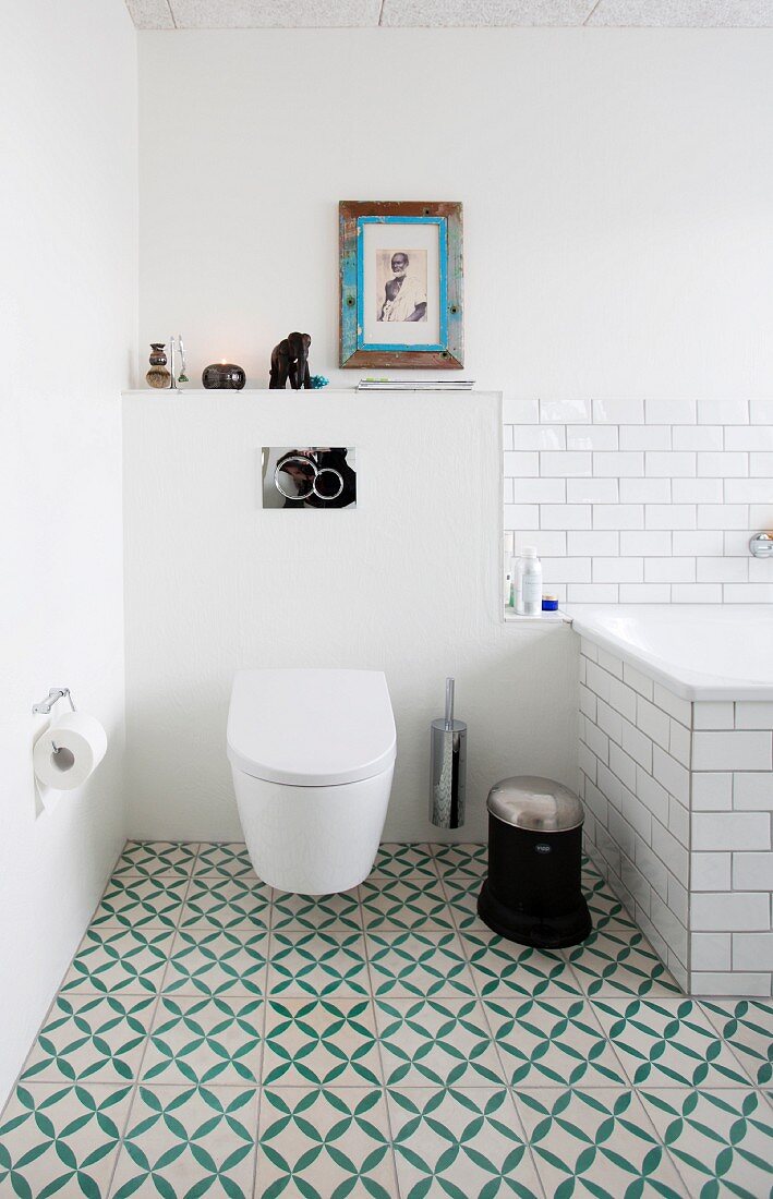 Toilet and bathtub in bathroom with green and white patterned floor tiles