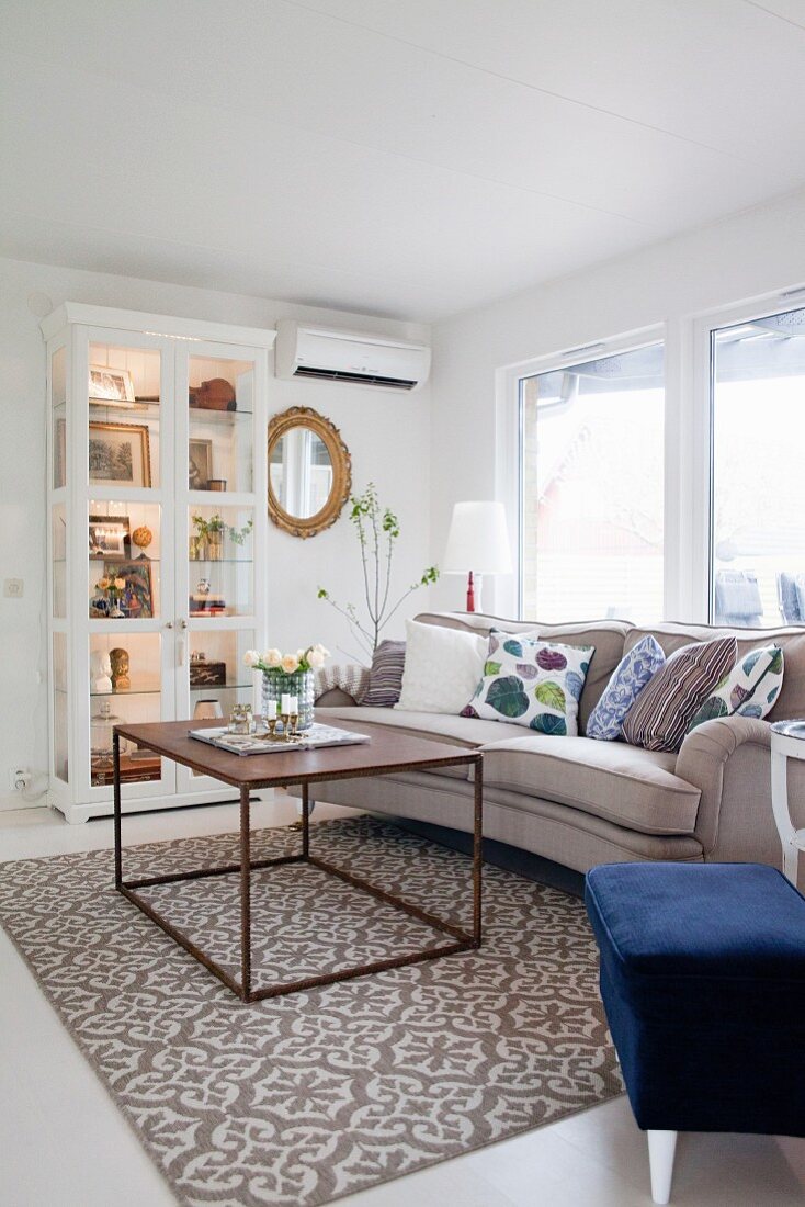 Cubic coffee table on patterned rug in front of sofa and display cabinet