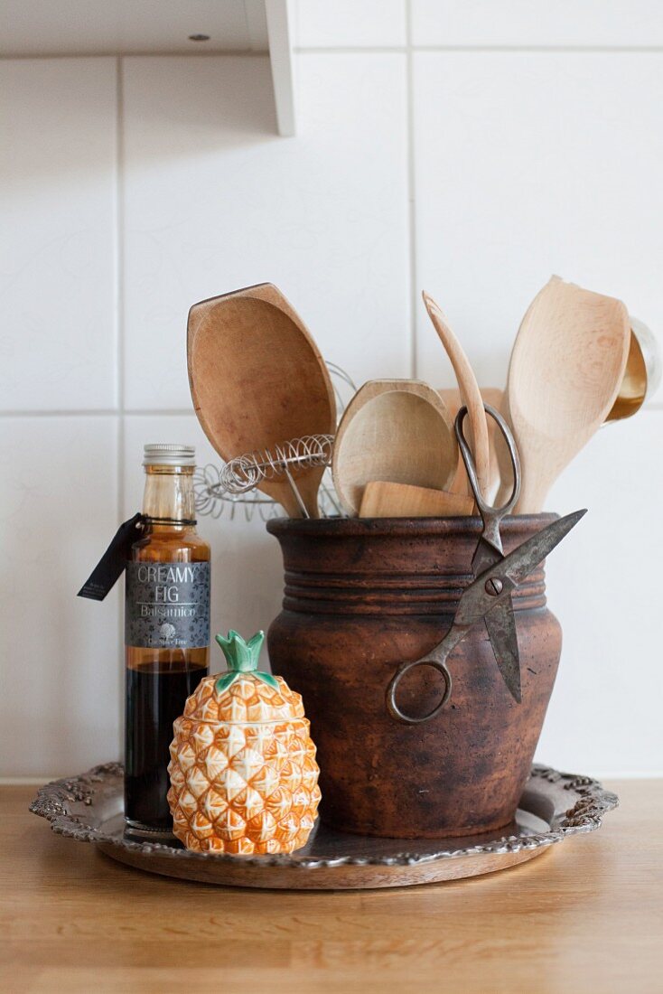 Küchenutensilien in einem rustikalen Tontopf und eine Deko-Ananas