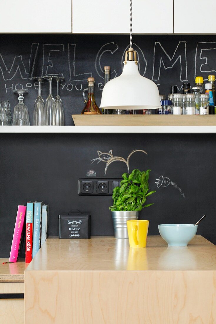 Kitchen counter with chalkboard splashback and white wall-mounted shelf