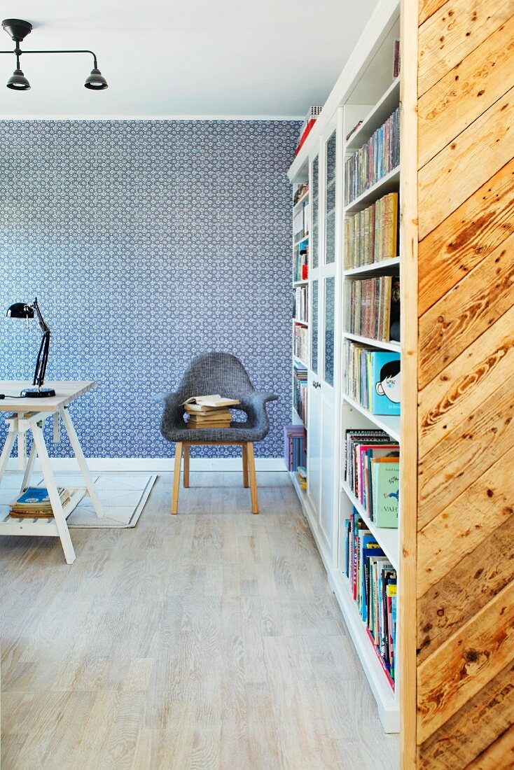 Bookcase and armchair in front of wall with blue and white wallpaper