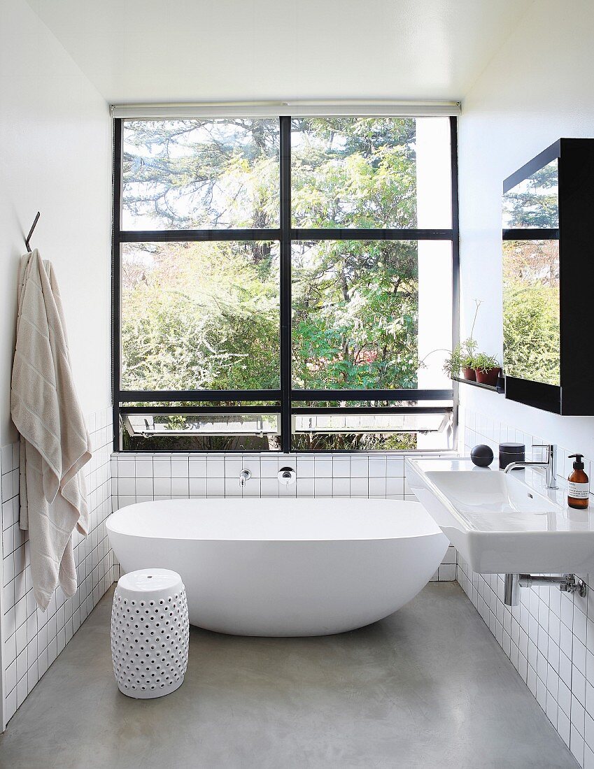 Free-standing bathtub and window with black frame in bright minimalist bathroom
