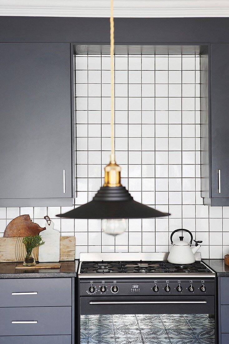 Black lampshade in front of grey fitted kitchen with white wall tiles and gas cooker