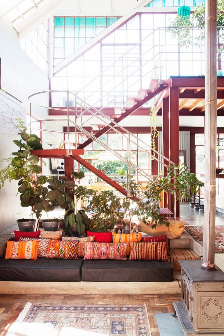 Gemütlicher Loungebereich mit orangefarbenen Kissen vor Treppe in Loftwohnung mit Glasfassade