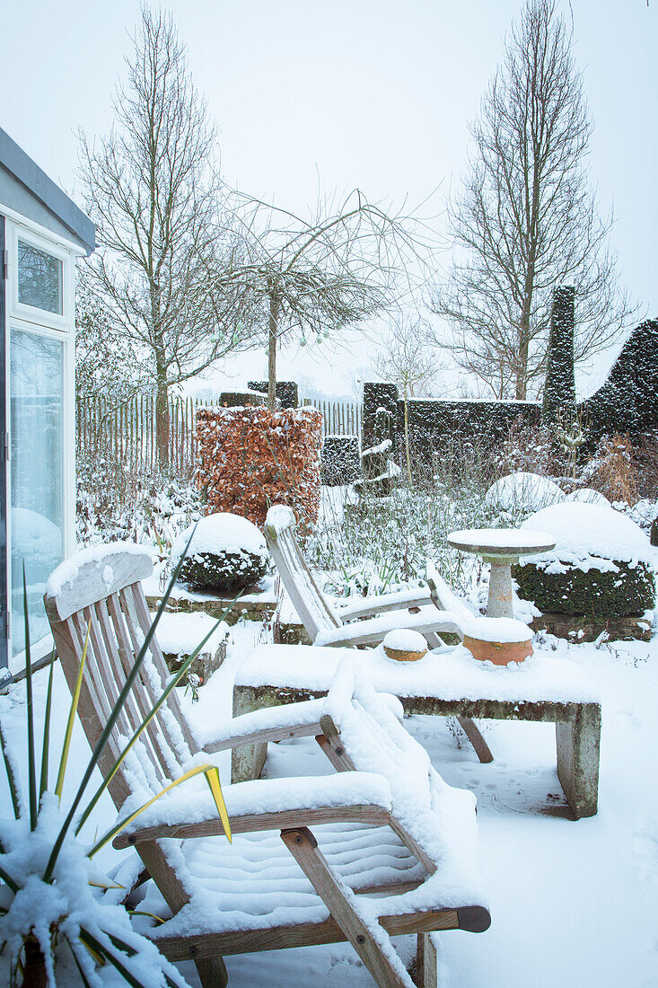 Garten im Winter mit Schneedecke und Holzmöbeln