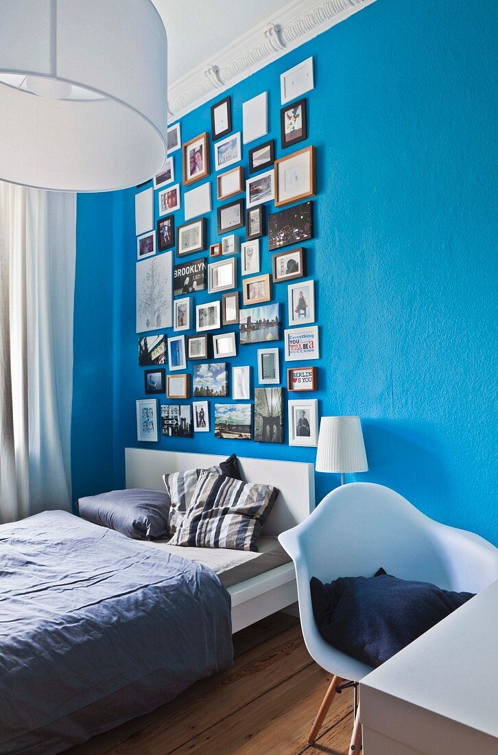 Verschiedene gerahmte Fotos in 'Petersburger Hängung' an blauer Wand in Schlafzimmer