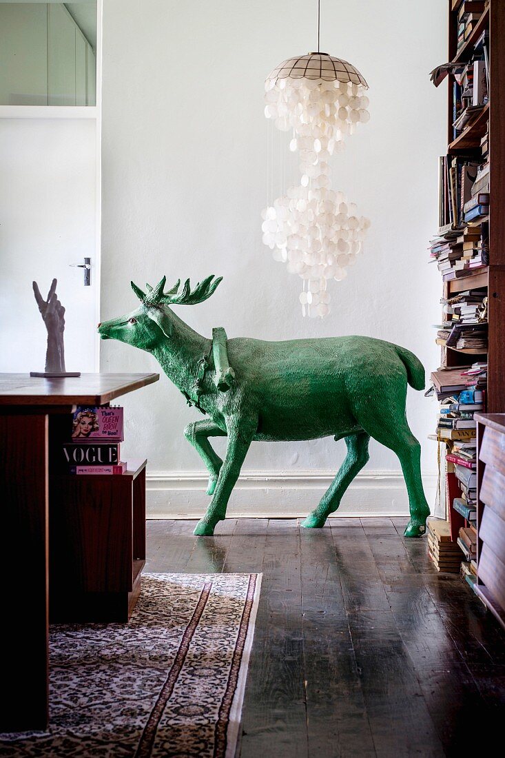 Grüne Hirschskulpturunter einer Muschellampe im Wohnzimmer