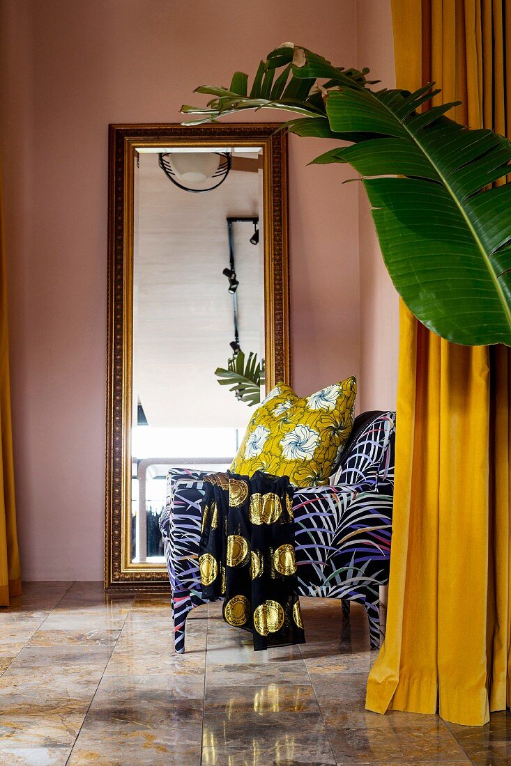 Patterned armchair in front of full-length mirror with large leaf in foreground