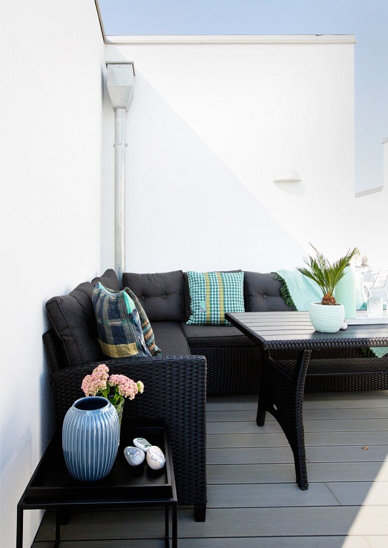 Schwarzes Überecksofa mit Sitzpolstern und Kissen vor weißer Wand auf sommerlicher Terrasse