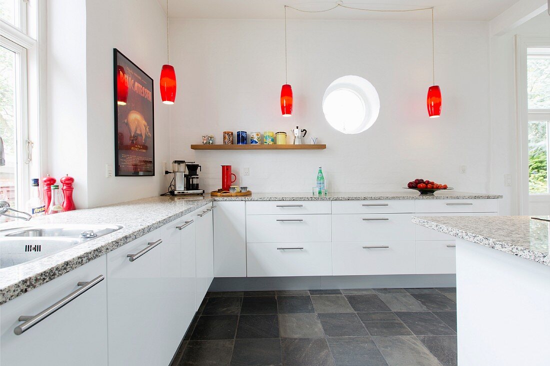 Schlichte, weiße Einbauküche mit Granit-Küchenarbeitsplatte und roten Retro-Pendelleuchten