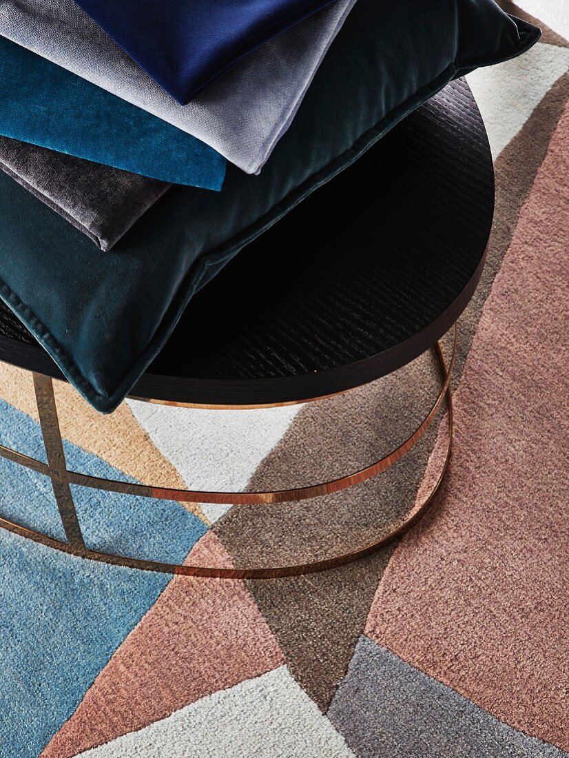 Stack of velvet cushions on stool on patterned rug