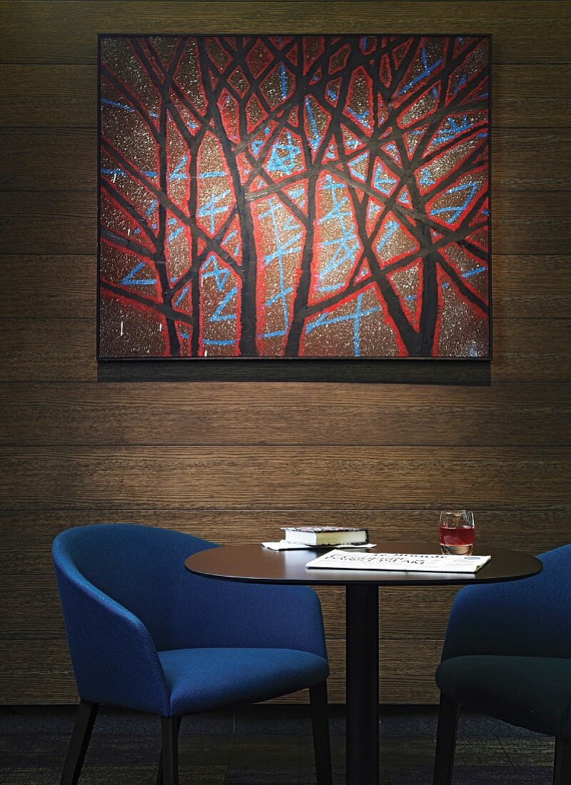 Zwei blaue Polsterstühle und Tisch vor Holzwand mit Gemälde
