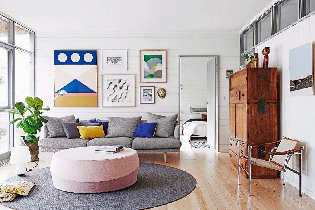 Graue Couch mit Kissen vor weißer, holzverkleideter Wand mit Bildergalerie in hellem Wohnzimmer