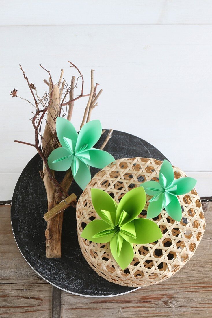 Green origami flowers on top of branch and basket