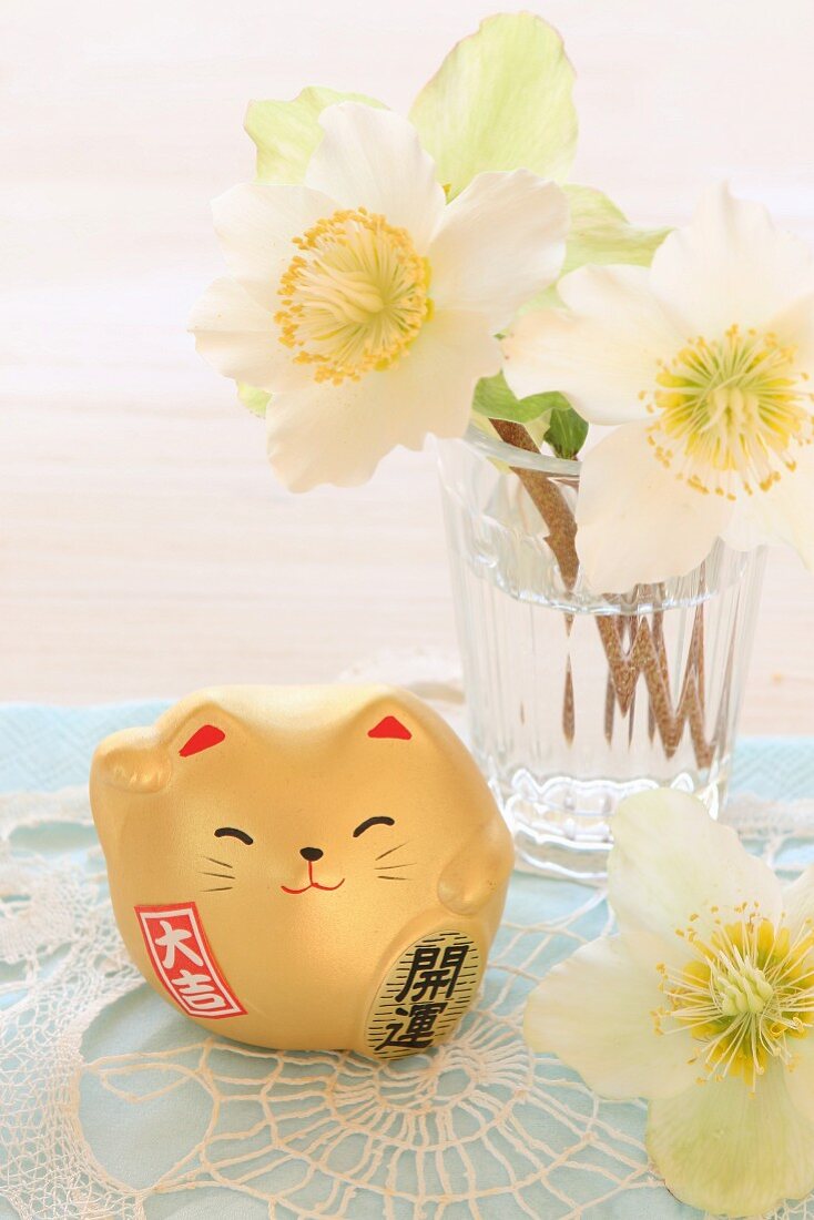 Chinesische Glücksbringer-Katze vor einem Glas mit Narzissen