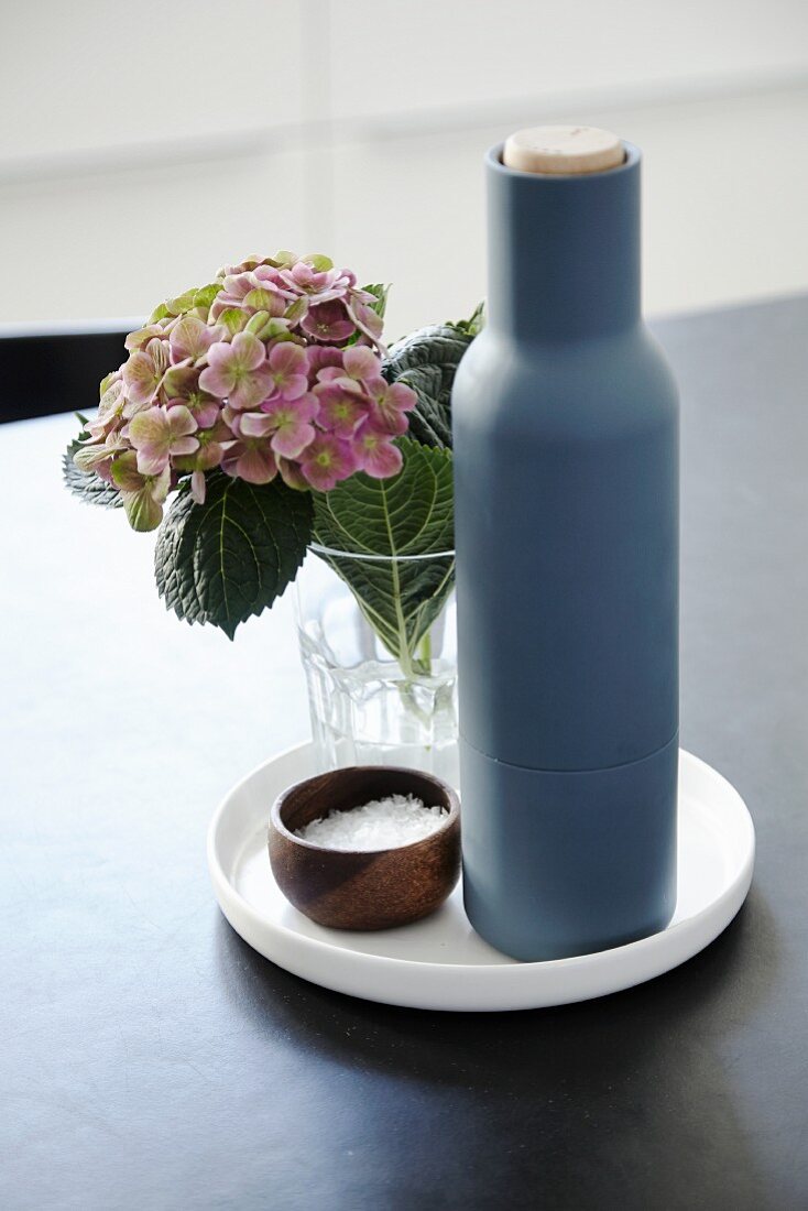 Blaue Flasche, Hortensie und Salztöpfchen auf weißem Teller