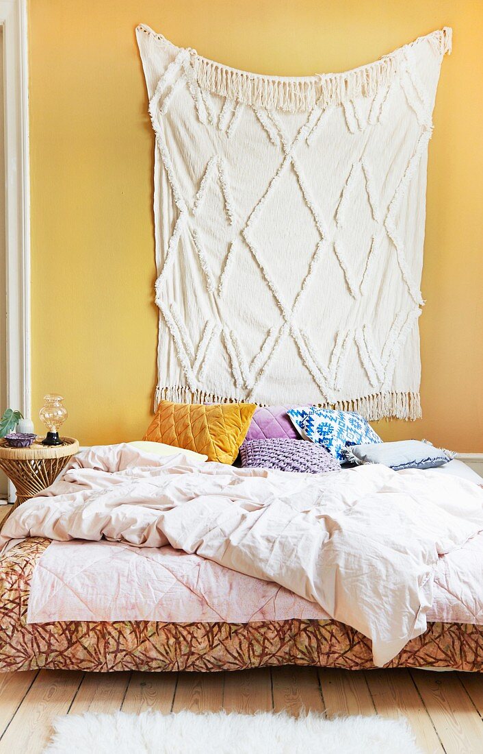 Cream fringed rug hung on yellow wall above bed