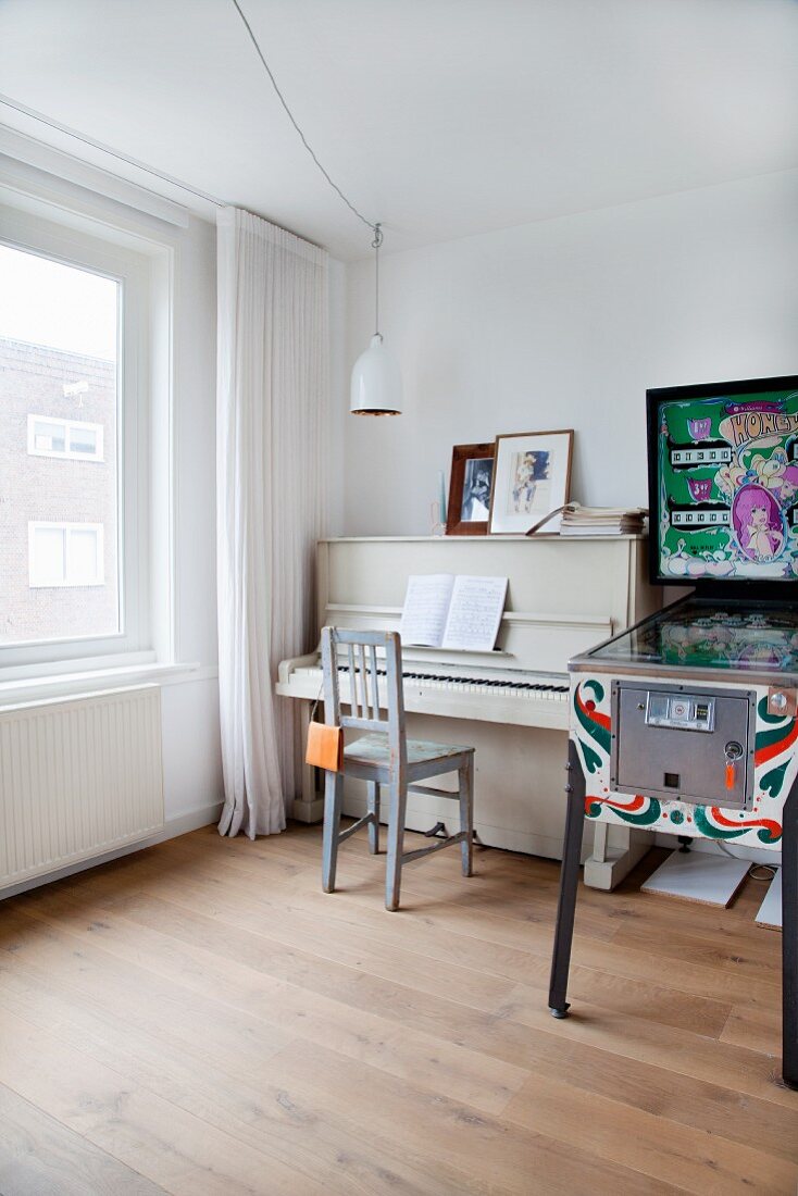 Piano and vintage chair next to colourful pinball machine