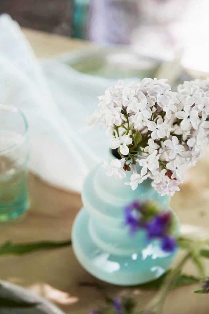 weiße Fliederblüten in türkisfarbener Vase auf Gartentisch