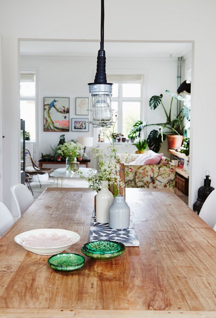 Rustikaler Tisch mit Keramikschalen und Blumenvasen, im Hintergrund Wohnbereich im skandinavischen Stil