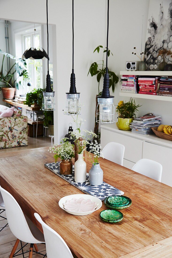 Rustikaler Tisch mit Keramikschalen und Blumenvasen, darüber Pendelleuchten im Industriestil