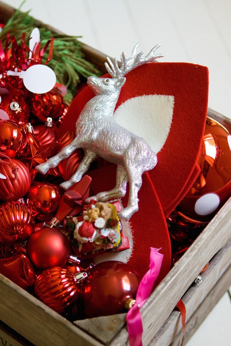 Holzkiste mit Deko-Hirsch und rotem Weihnachtsschmuck