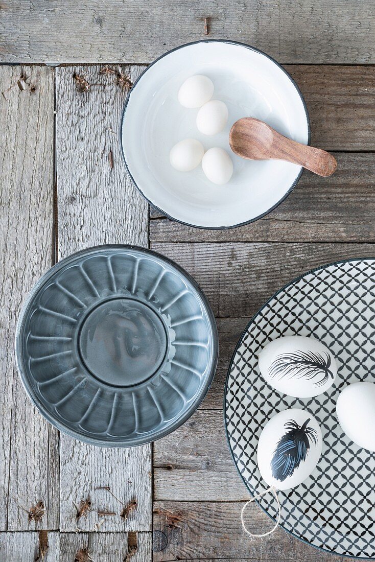 Eggs painted with feather on patterned plate and bowls on wooden surface