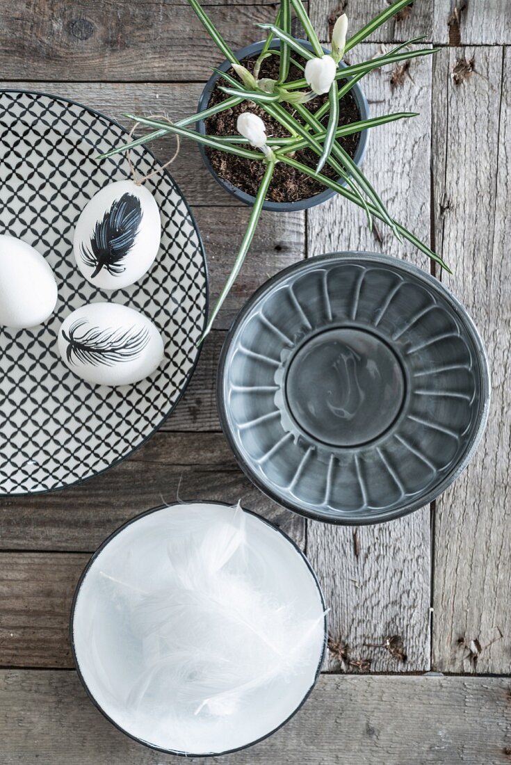 Eggs painted with feather on patterned plate and bowls on wooden surface