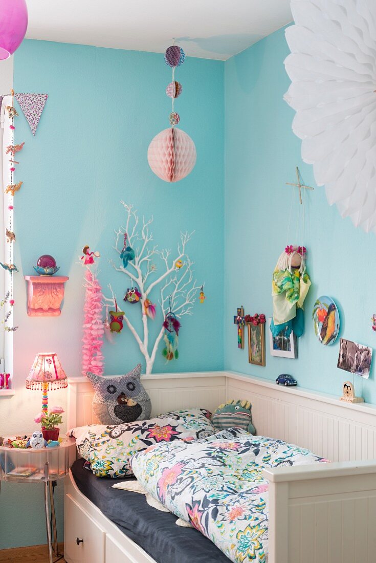 Hellblaue Wand im Kinderzimmer mit bunter Deko über dem Bett