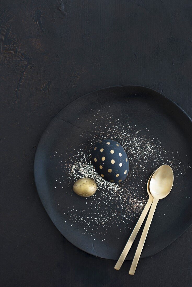 Glitter, gold spoon and gold and black Easter eggs on black plate