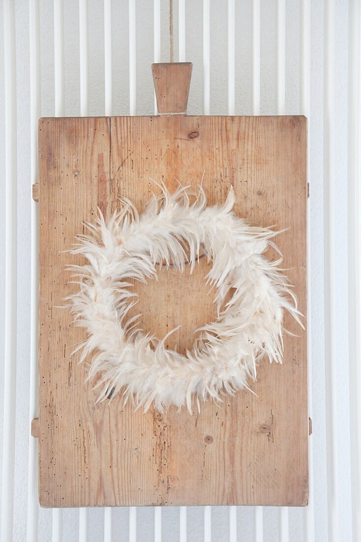 Wreath of feathers on old chopping board hung on radiator