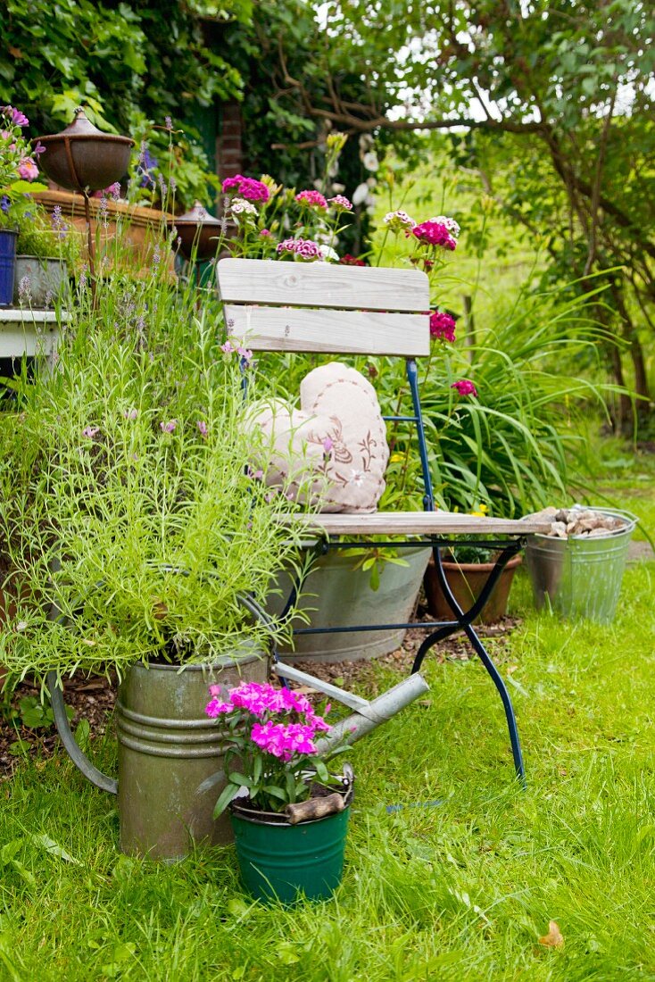 Mit Blumen bepflanzte Gießkanne neben einem Stuhl im Garten